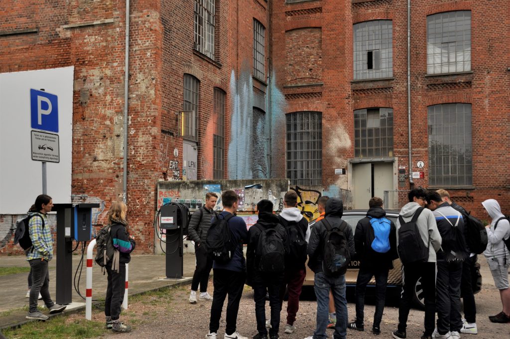 Man sieht eine Gruppe von Schüler*innen vor einem E-Auto das bidirektional laden kann