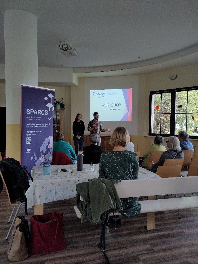 Auf dem Bild sieht man den Workshopraum bei der Energiesprechstunde im Dunckerviertel. Man sieht, wie dem Publikum Folien zu dem Workshop gezeigt werden.